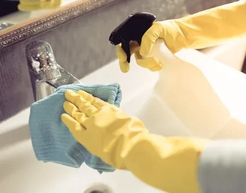 Cleaner in yellow gloves wiping a bathroom sink and faucet during a detailed deep cleaning